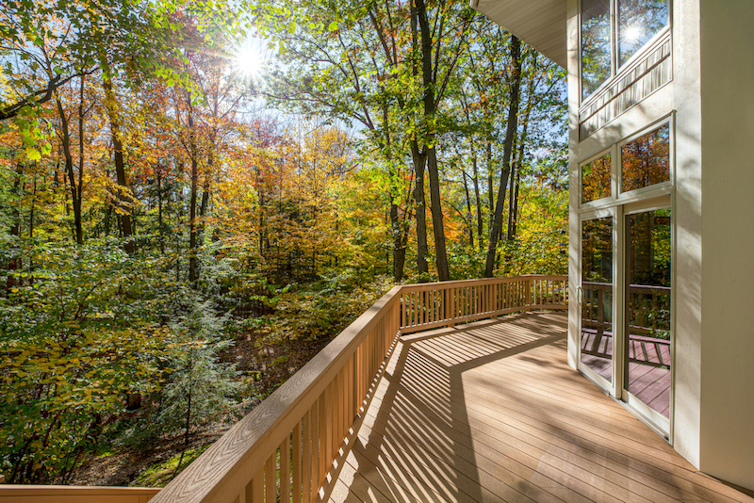 View from the deck of a luxury home in the autumn woods.  Outdoor living concept, bright fall foliage, and intentional sun flare highlight. (View from the deck of a luxury home in the autumn woods.  Outdoor living concept, bright fall foliage, and int