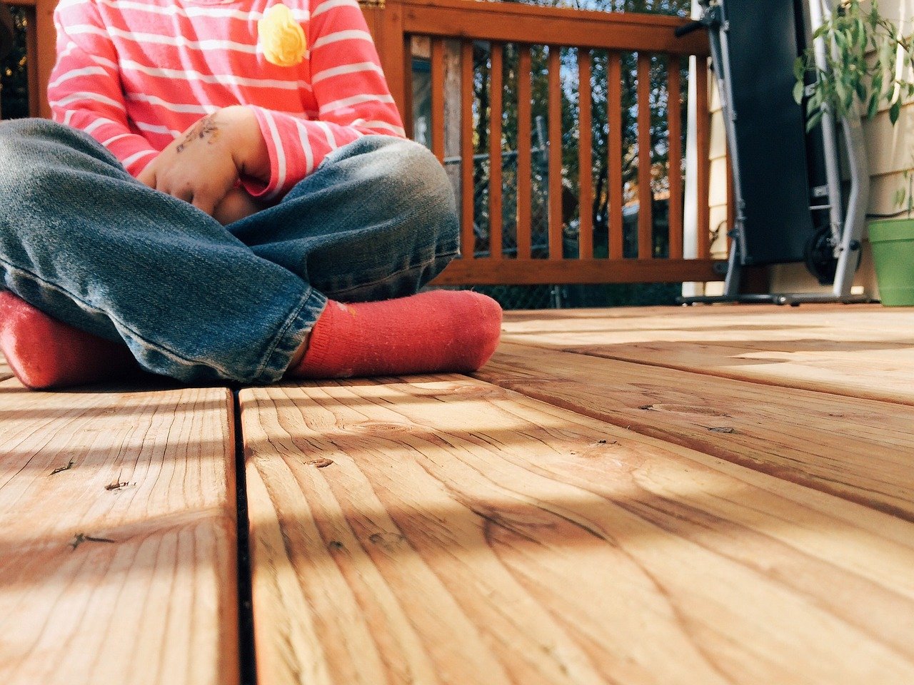 Small child in red shirt sitting on sunny deck